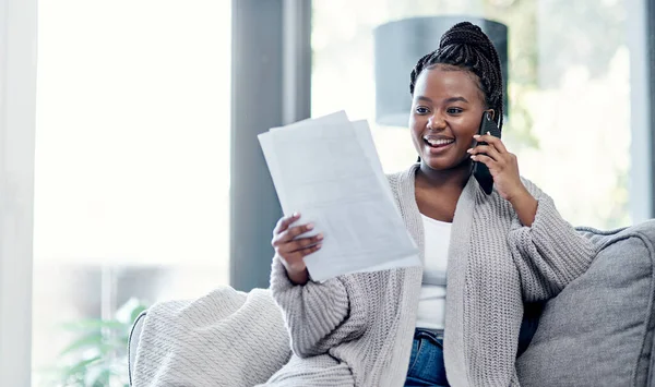 Goed financieel advies is slechts een telefoontje verwijderd. Foto van een jonge vrouw die papierwerk bekijkt en een smartphone op de bank thuis gebruikt. — Stockfoto