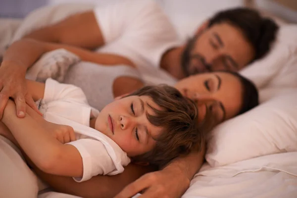 Ele quer estar sempre perto da mamã e do papá. Tiro cortado de uma jovem família na cama juntos. — Fotografia de Stock