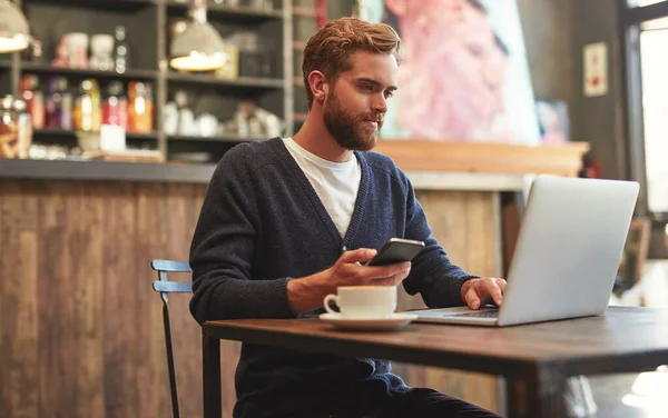 技術は彼にどこでも働く自由を与える。カフェでノートパソコンと携帯電話を使って若い男のショット. — ストック写真