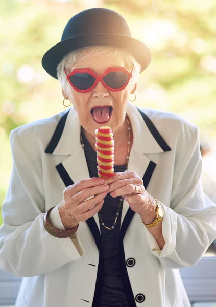 Haar innerlijke kind hunkert naar ijs. Portret van een vrolijke oudere vrouw die buiten een ijsje eet. — Stockfoto