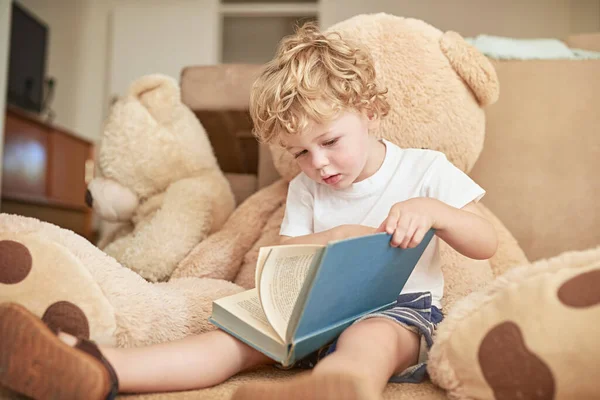 Se está convirtiendo en un lector entusiasta. Foto de un adorable niño leyendo con su osito de peluche en casa. — Foto de Stock