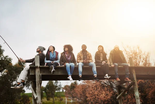 Mengumpulkan momen, bukan hal-hal. Shot of a group of friends sitting on a pier together on a weekend breakaway. — Stok Foto