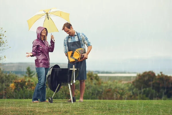 Hacemos barbacoas en cualquier momento, en cualquier lugar. Toma de una pareja felizmente asando bajo la lluvia. — Foto de Stock