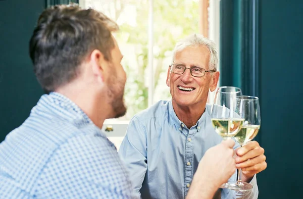 Hier zijn jij en mijn vader. Shot van een vrolijke oudere man en zijn zoon delen een feestelijke toast met wijnglazen thuis. — Stockfoto