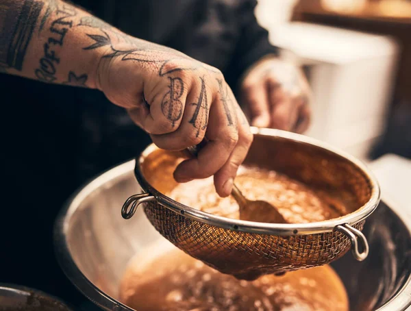 Ce plat est assommant. Gros plan d'un chef méconnaissable tatoué mains filtrant la nourriture dans un bol dans la cuisine d'un restaurant. — Photo