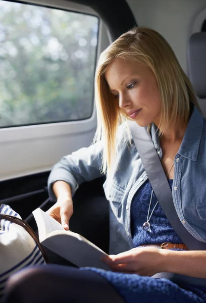 Czas nadrobić zaległości w czytaniu. Strzał młodej kobiety czytającej książkę na tylnym siedzeniu samochodu podczas podróży.. — Zdjęcie stockowe
