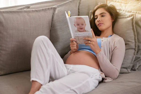Preparando-se para a jornada através da maternidade. Tiro de uma jovem grávida lendo um livro de bebê em casa. — Fotografia de Stock