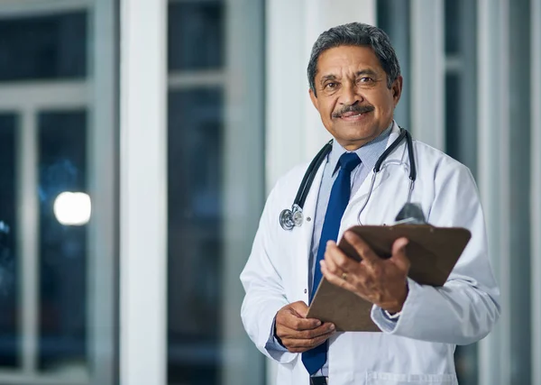 Le docteur est là. Portrait d'un médecin mature heureux tenant un presse-papiers dans un hôpital. — Photo