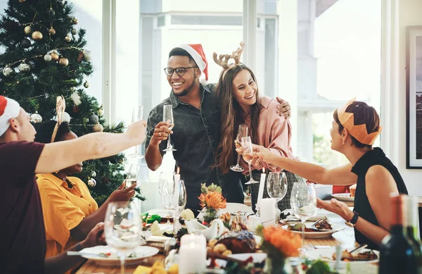 Salud por tu primer almuerzo de Navidad juntos. Recorte de una alegre pareja joven brindando con sus amigos mientras almuerzan en casa. — Foto de Stock