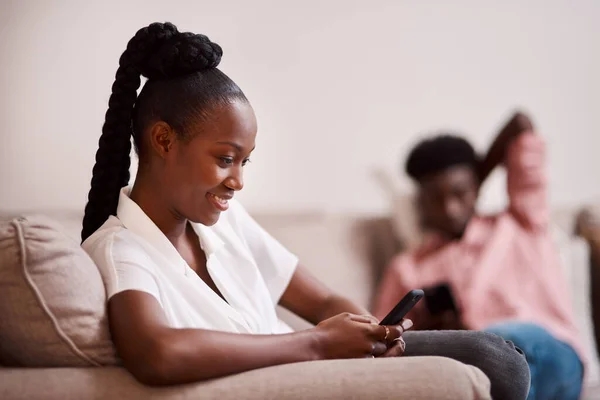 Prefiero estar desplazándome de todos modos. Desenfocado de una mujer usando su teléfono celular mientras su pareja se sienta en el fondo. — Foto de Stock