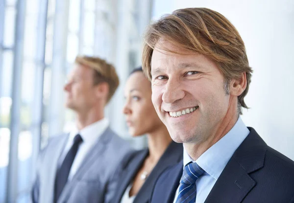 Un día estaré en el top 50 de Fortune 500. Un empresario sonriente con dos compañeros de trabajo detrás de él. —  Fotos de Stock