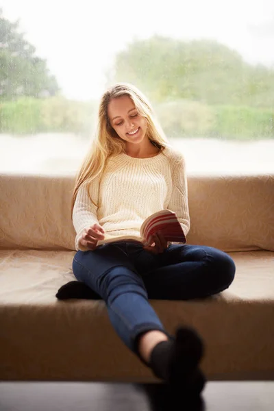 Пусть твой разум погрузится в хорошую книгу. Фотография привлекательной молодой женщины, читающей книгу, сидя дома на диване. — стоковое фото