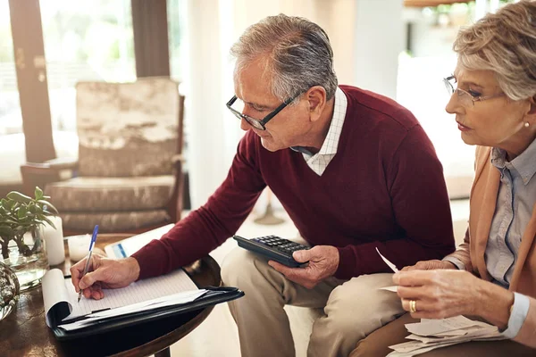 Ik hou nota van al onze uitgaven. Opname van een bejaard echtpaar dat een budget aan het uitwerken is terwijl ze op de zitbank zitten. — Stockfoto