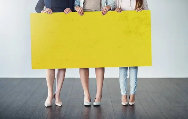 Attendete un messaggio dagli affari. Colpo ritagliato in studio di un gruppo di donne d'affari che reggono un cartello giallo vuoto. — Foto Stock
