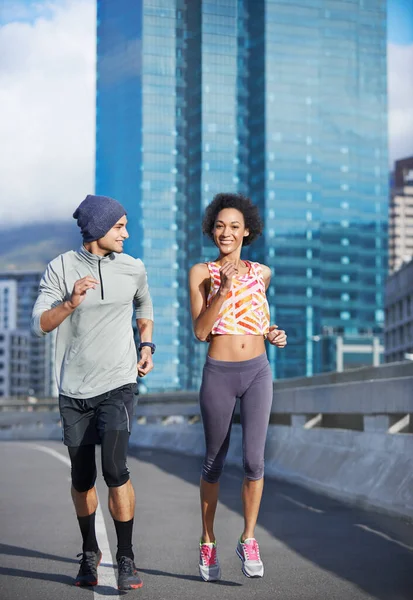 He almost keeps pace with me. Shot of two friends jogging together through the city streets. — Stock Photo, Image
