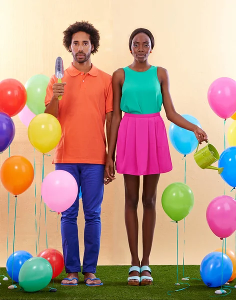 Feeling a bit out of place.... An awkward african couple surround by colorful balloons while holding hands. — ストック写真