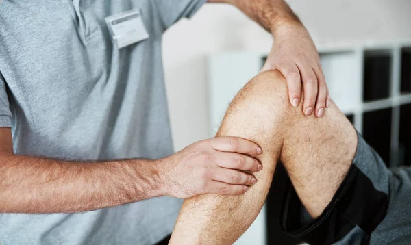 Hará que el dolor desaparezca. Foto de un fisioterapeuta masculino irreconocible ayudando a un cliente con ejercicios de piernas que yace en una cama. —  Fotos de Stock