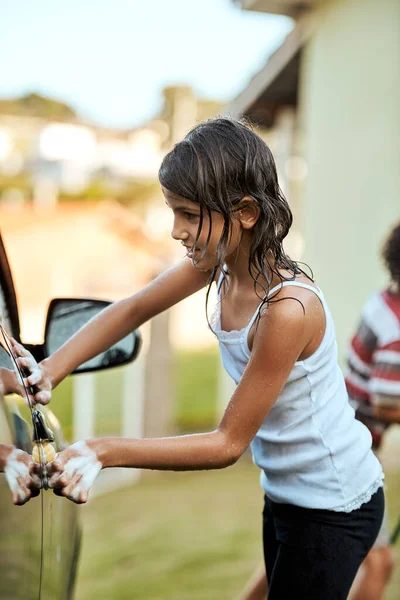 スポットを逃さないようにしないと。日中に両親の車を外で洗っている陽気な女の子のショット. — ストック写真