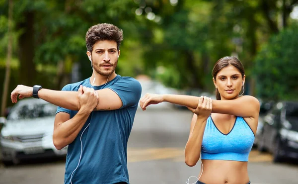 A aptidão é o nosso desafio para conquistar juntos. Retrato de um jovem casal esportivo se alongando enquanto exercitam juntos ao ar livre. — Fotografia de Stock