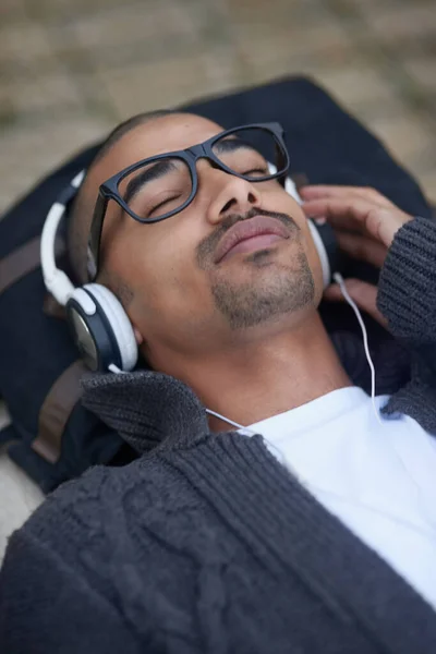 Det perfekta soundtracket för att lindra hans stress. Beskuren bild av en collegestudent som lyssnar på musik på hörlurar på campus. — Stockfoto