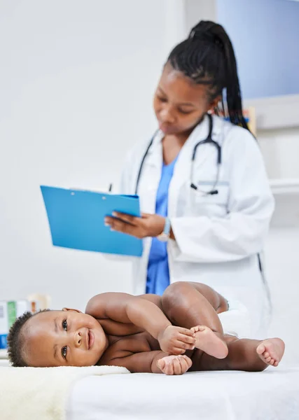 Es ist ein vollkommen gesundes Baby. Aufnahme einer Ärztin, die Notizen über ihren kleinen Patienten auf einem Klemmbrett macht. — Stockfoto