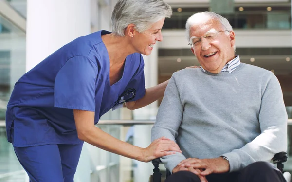 O riso é como umas férias instantâneas. Tiro cortado de um homem idoso feliz sentado em uma cadeira de rodas, enquanto sua ajuda enfermeira madura atraente ajuda-o dentro de casa. — Fotografia de Stock