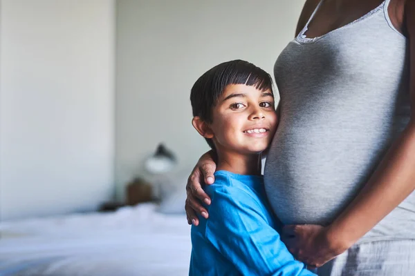 Soon there will be three of us. Cropped portrait of an adorable little boy standing against his mothers pregnant belly. — Stock Photo, Image