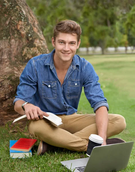 This is better than the library. Portrait of a handsome young man studying in the park with a laptop. — ストック写真