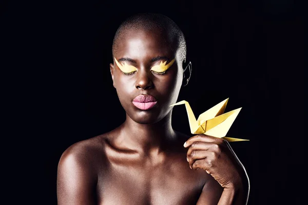 Sie ist eine wahre Königin Afrikas. Schnappschuss einer schönen ethnischen Frau, die mit geschlossenen Augen posiert, während sie einen Origami-Vogel hält. — Stockfoto