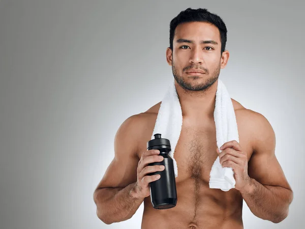 Wenn es schlimm genug ist, schwitzt man dafür. Aufnahme eines athletischen Mannes mit einer Wasserflasche vor grauem Hintergrund. — Stockfoto