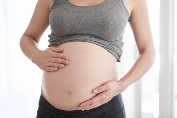 Mostrando su barriga. Foto recortada de una mujer embarazada de pie en su casa. — Foto de Stock