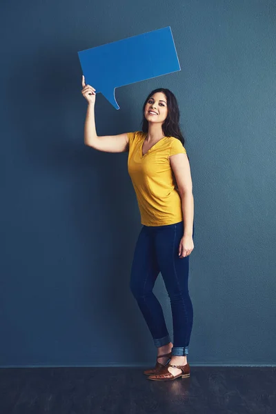 Capacite a sua voz. Retrato de estúdio de uma jovem atraente segurando uma bolha de fala contra um fundo azul. — Fotografia de Stock