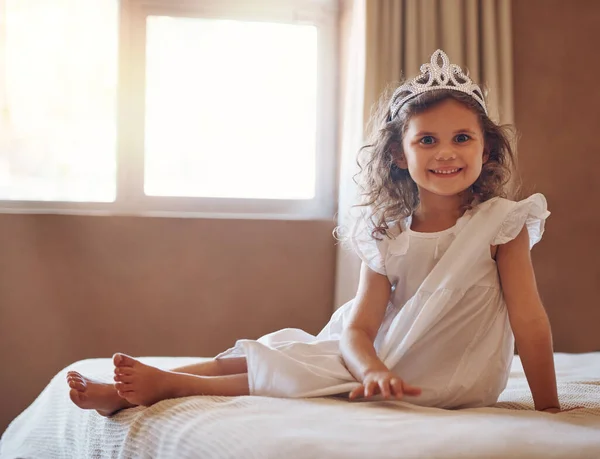 Δεν είναι απλά η πιο χαριτωμένη πριγκίπισσα που έχεις δει ποτέ; Πορτρέτο ενός αξιολάτρευτου μικρού κοριτσιού που φοράει τιάρα και κάθεται σε ένα κρεβάτι στο σπίτι. — Φωτογραφία Αρχείου