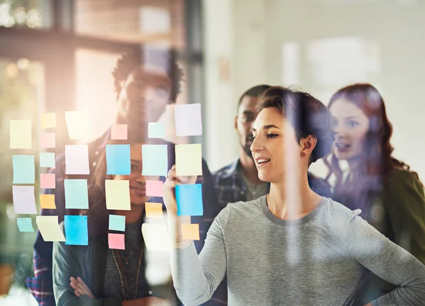 She has their plans all mapped out. Cropped shot of coworkers using sticky notes on a glass wall during an office meeting. — Stock Photo, Image