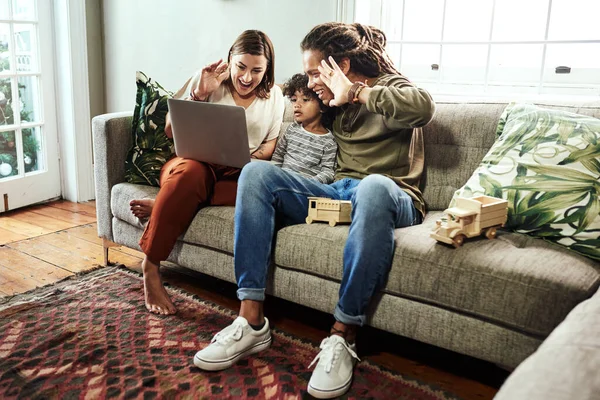 Χαιρέτα την κάμερα. Φωτογραφία ενός χαρούμενου νεαρού ζευγαριού και του γιου τους να έχουν βιντεοκλήση σε συγγενείς σε φορητό υπολογιστή ενώ κάθονται σε καναπέ στο σπίτι. — Φωτογραφία Αρχείου
