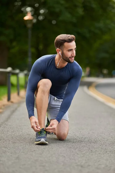 Atado y listo para salir. Largura completa de un guapo joven corredor atándose los cordones de los zapatos durante un entrenamiento al aire libre. — Foto de Stock