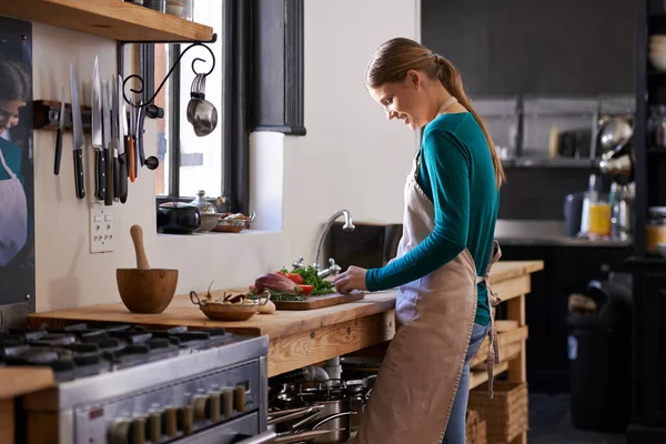 Es una profesional en la cocina. Tiro de una joven mujer picando verduras en un mostrador de cocina. — Foto de Stock