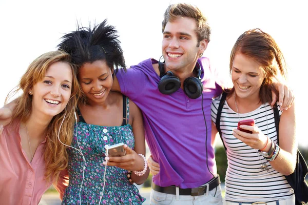 Partilhar música e fotografias com os meus amigos. Fechamento de quatro amigos ouvindo música e digitando em seus celulares. — Fotografia de Stock