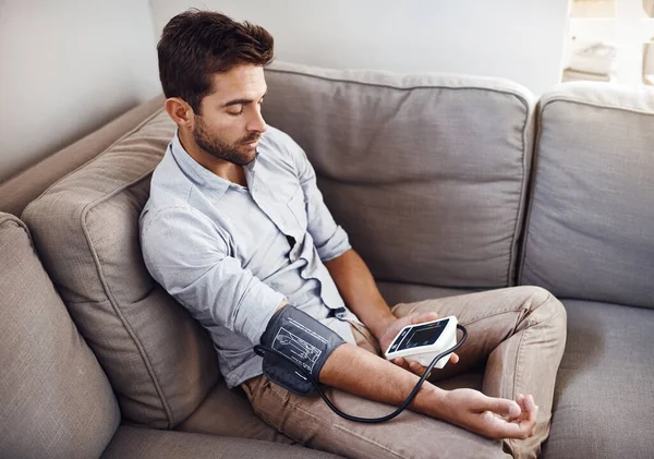 Doing my regular checkup. Shot of a young man taking his own blood pressure readings with a blood pressure monitor at home. — Stock Photo, Image