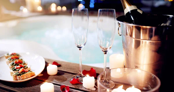 This is where you want to come celebrate your love. Shot of a beautiful setting of champagne and treats near a hot tub at night. — Stock Photo, Image