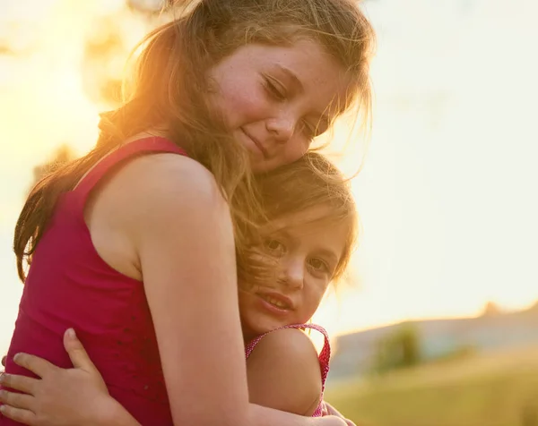 자매들 과 친구들. 귀여운 여자 아이 가 공원에서 노는 동안 동생을 안아 주는 장면. — 스톡 사진