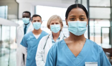 Tıbbi profesyoneller olarak yapmamız gereken çok önemli bir iş var. Hastanede yan yana dururken yüz maskesi takan bir grup tıp doktorunun portresi..