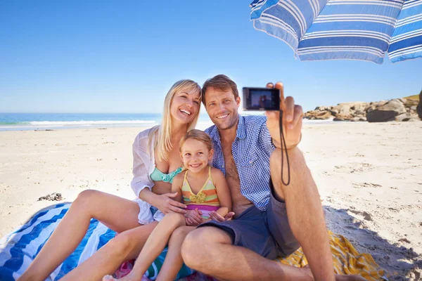 Smiling for a holiday pic. Shot of a happy young family taking a photo of themselves at the beach. — Stock Photo, Image