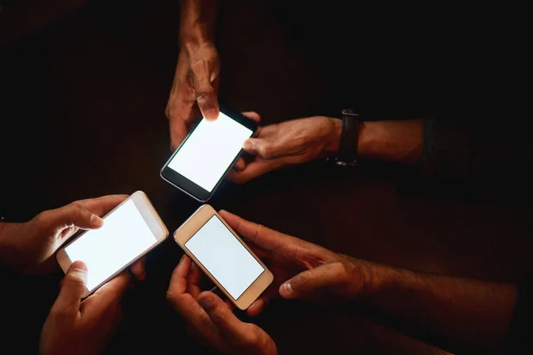 A fazer planos juntos como um chefe. Close-up de um grupo de pessoas irreconhecíveis mensagens de texto em seus telefones enquanto estão sentados dentro de um bar à noite. — Fotografia de Stock