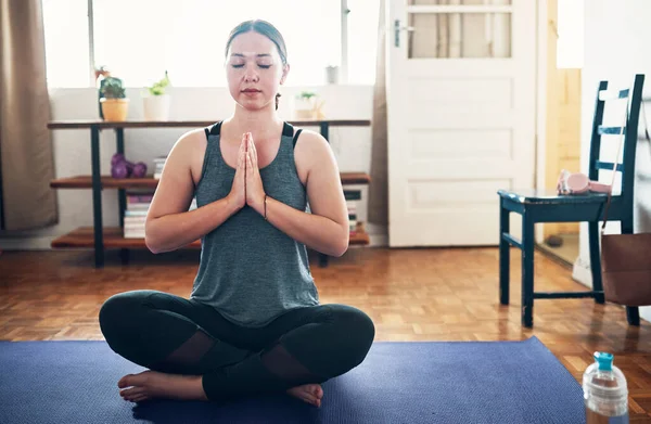 Concentrándome en mi respiración. Foto recortada de una atractiva joven sentada en una esterilla de yoga y meditando sola en su casa. — Foto de Stock