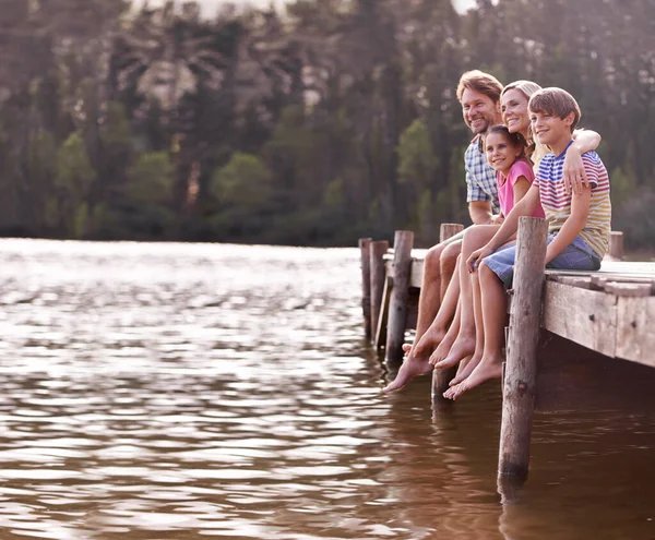Yıllık aile gölü tatili gibisi yok. Dört kişilik mutlu bir aile gölde bir iskelede oturuyor.. — Stok fotoğraf