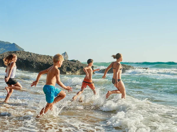 Det er ikke det perfekte øyeblikket, gå nå. Skutt av søsken som løp ut i vannet på stranden på en solrik dag. – stockfoto