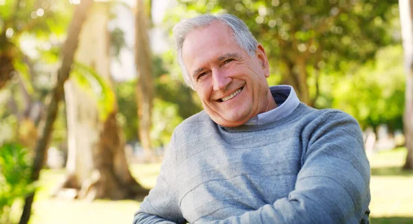 Im Endeffekt bereut er es nicht. Zugeschnittenes Porträt eines glücklichen Seniors, der allein im Park sitzt. — Stockfoto