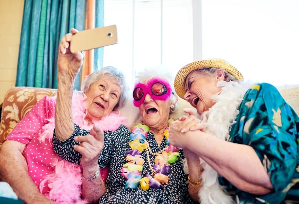 Como é que isto funciona? Tiro de um grupo de idosos despreocupados vestindo trajes funky e chegando perto para uma selfie dentro de um edifício. — Fotografia de Stock