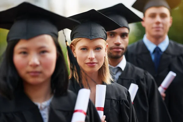 Dit is het begin, van alles wat je wilt. Een groep afgestudeerden die in pet en toga staan en hun diploma 's vasthouden. — Stockfoto